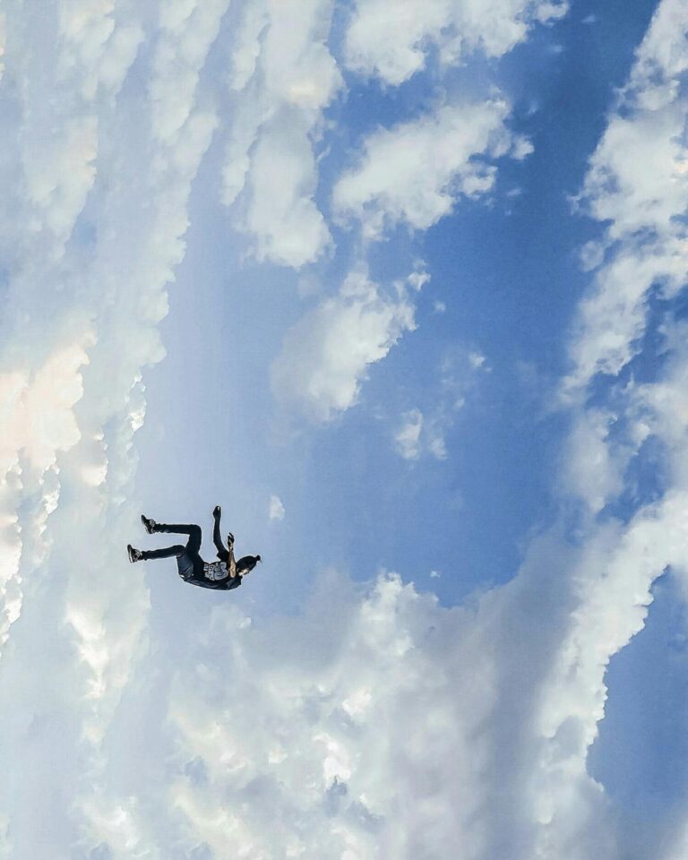 Eine Person schwebt in der Luft zwischen Wolken und blauem Himmel.