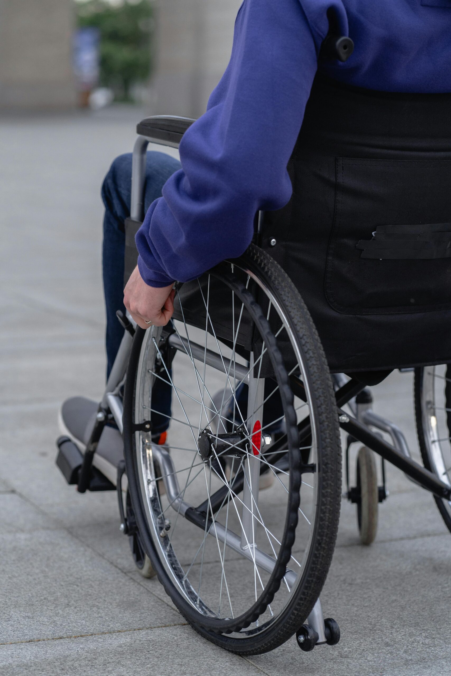 Eine Person sitzt in einem Rollstuhl und greift nach dem Rad, während sie auf einem Gehweg steht.